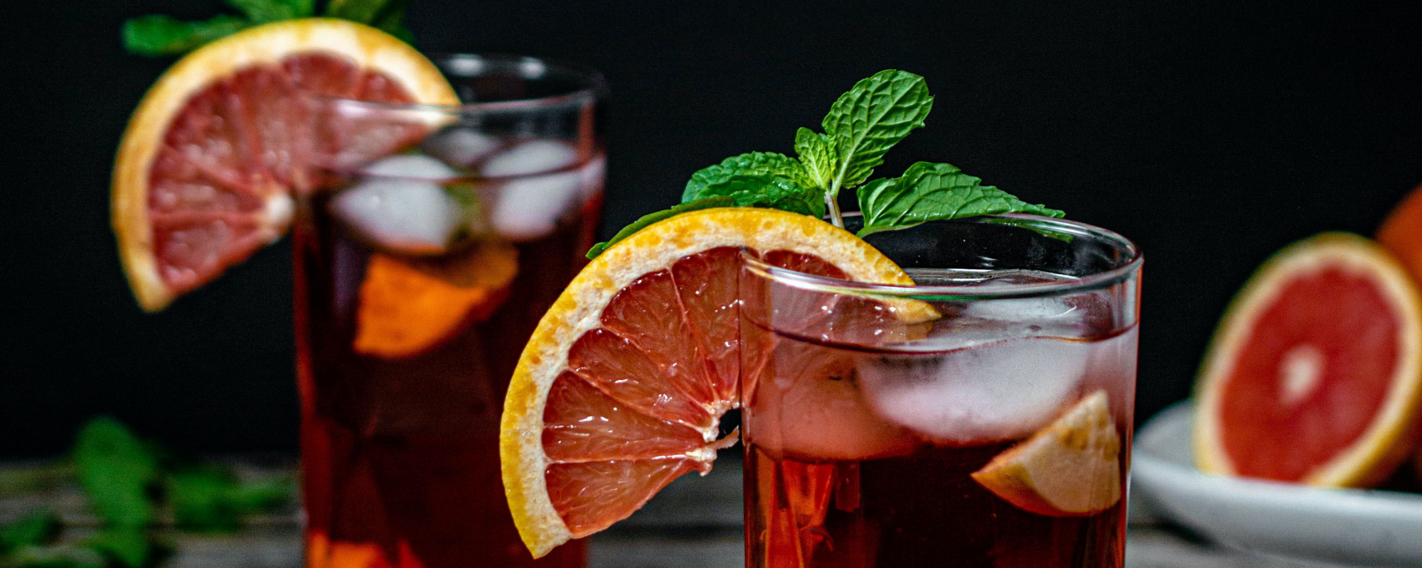 two mixed drinks with an orange and mint garnish 